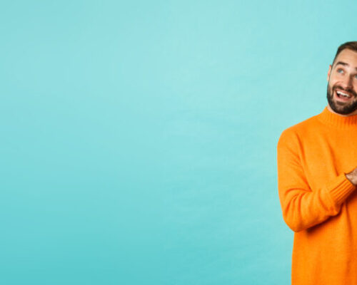 Handsome man thinking and using digital tablet, shopping online and pondering ideas, looking at upper left corner, standing over light blue background